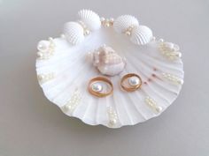 a shell with two rings and pearls on it, sitting on a table next to a pair of earrings