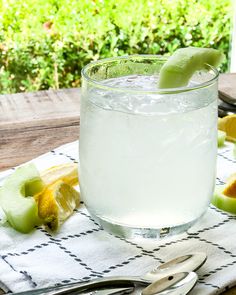 a glass filled with water sitting on top of a table next to sliced kiwis