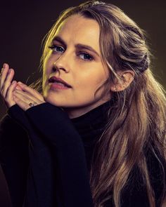 a woman with long hair wearing a black sweater and posing for a photo in front of a dark background