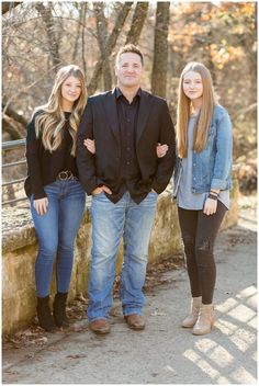 three people standing next to each other in front of trees