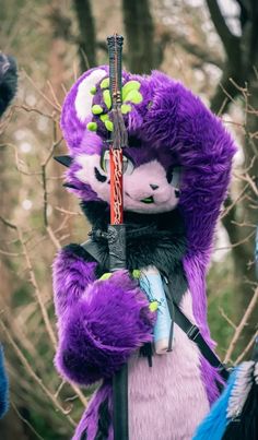 a purple stuffed animal holding a stick in its hands