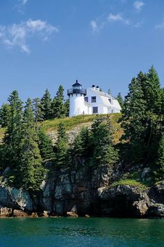 a white house on top of a hill next to the ocean with trees around it