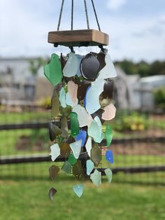 a wind chime made out of sea glass on a wire and wood stand in front of a fence