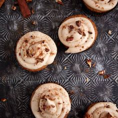 several cupcakes with white frosting and nuts on a metal tray next to cinnamon sticks