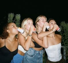 four young women are drinking and laughing together at the same time, while one woman is wearing a white top