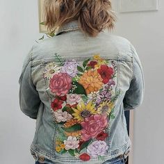 a woman wearing a jean jacket with flowers painted on the front and back of it