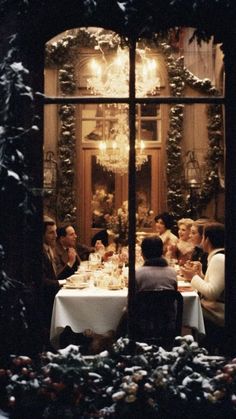 a group of people sitting at a table in front of a window with christmas decorations on it