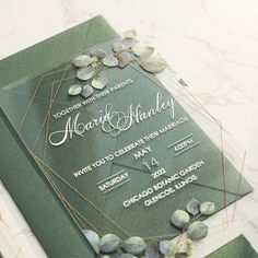 a green wedding card with flowers on the front and back, sitting on a marble table