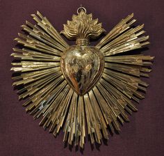 an ornate gold heart shaped object on a purple surface with other items around it and the shape of a sunburst in the center