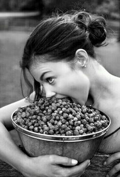 a woman is biting into a basket full of raspberries in black and white