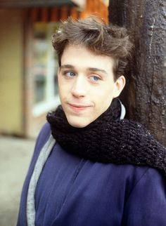 a man standing next to a tree wearing a scarf on his neck and looking at the camera