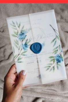 a person holding an open wedding card with blue flowers on it and a wax stamp