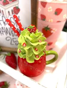 a red mug with green frosting and strawberries on it sitting on a shelf