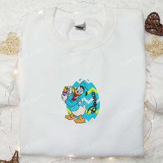 Introducing our adorable Donald Duck With Easter Chick Embroidered Shirt! This charming Disney-inspired shirt showcases a delightful embroidery of Donald Duck holding a cute Easter chick. Made with high-quality materials, it offers superior comfort and durability. With its vibrant colors and meticulous detailing, this shirt is perfect for Disney enthusiasts of all ages. Whether you’re [...] Chick Shirt, Disney Donald Duck, Perfect Thanksgiving, Bustling City, Easter Chick, Best Mothers Day Gifts, Cartoon Gift, St Patrick's Day Gifts, Sports Hoodies