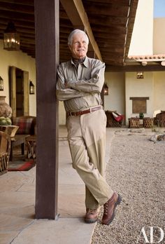 an older man leaning on the side of a building with his arms crossed and looking at the camera