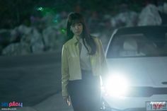 a woman standing next to a car in the street at night with her headlight on