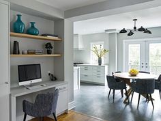 a dining room table with chairs and a computer monitor on top of it, in front of open shelves