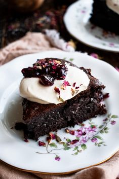 a piece of chocolate cake on a plate with whipped cream and flowers around the edge