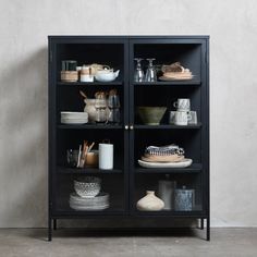 a black cabinet with glass doors and dishes on it's shelves in front of a white wall