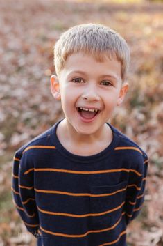 a young boy is smiling and posing for the camera in front of some fallen leaves