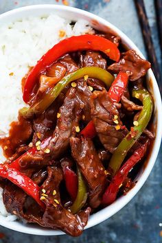 a white bowl filled with beef and peppers on top of rice next to chopsticks