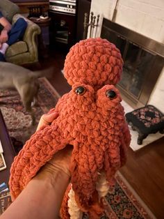 an orange crocheted octopus stuffed animal being held in front of a fire place