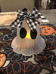 a white bell with a black bow on it sitting on top of a table covered in pumpkins