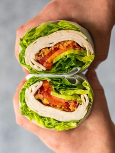 two sandwiches with lettuce, bacon and tomato on them being held by someone's hand