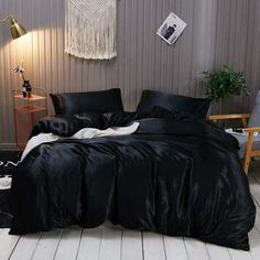 a bed with black sheets and pillows in a room next to a lamp on the floor