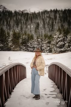 a woman is standing on a bridge in the snow wearing jeans and a cowboy hat