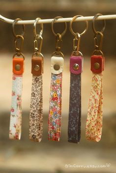 four key chains hanging from a clothes line with flowers on them, all in different colors