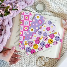 a person holding an open book on top of a white blanket next to flowers and other items