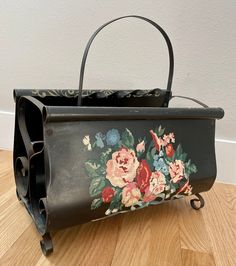 an old black purse with flowers painted on the side and handles sitting on a wooden floor