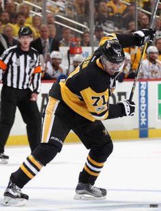 a hockey player in black and yellow uniform skating on the ice with an official referee behind him