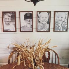 a wooden table topped with a vase filled with wheat next to pictures on the wall