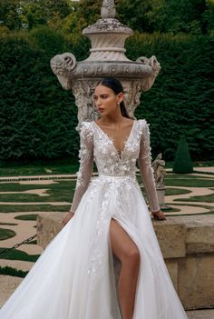 a woman in a white wedding dress standing next to a fountain with her legs crossed