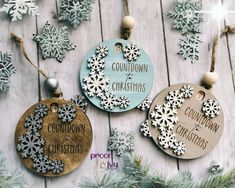 three wooden ornaments with snowflakes hanging from them on a wood table next to christmas decorations