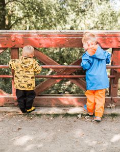 two little boys standing next to each other near a wooden fence with trees in the background