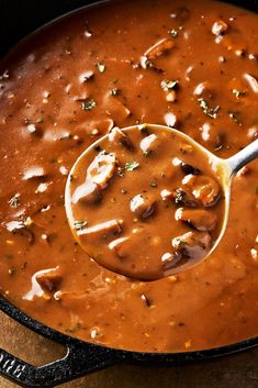 a ladle full of soup is being stirred by a wooden spoon in a skillet