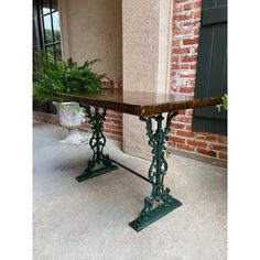 a table that is sitting in front of a brick building with green metal legs and wood top