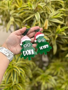 two green and red christmas tree ornaments in front of a bush with trees behind them