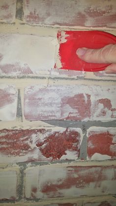 a person is painting a brick wall with red paint