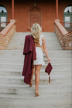 a woman is walking down the stairs with her graduation robe over her shoulders and holding a red purse