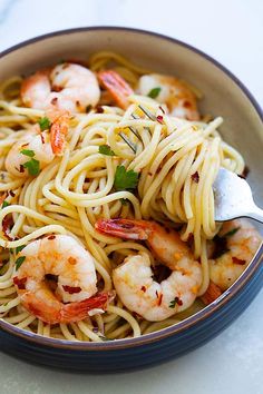 a bowl filled with pasta and shrimp on top of a white countertop next to a fork