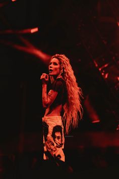 a woman standing on top of a stage with her hands in her pockets while holding a microphone