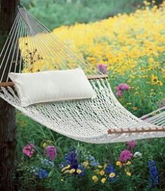 a white hammock hanging from a tree in a field full of wildflowers