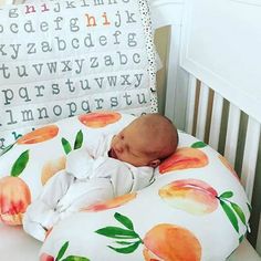 a baby sleeping in a crib next to a pillow with peaches on it