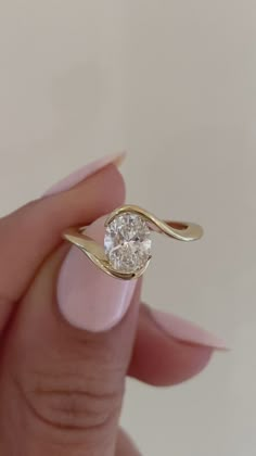 a woman's hand holding a gold ring with a diamond in the middle and a white background