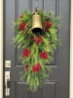 a christmas wreath with pine cones, berries and bells hanging on the front door handle