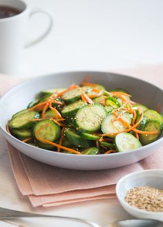 a bowl filled with cucumbers and carrots next to a cup of coffee